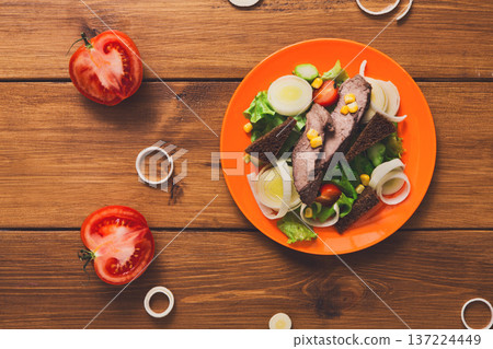 Healthy eating concept. Fresh salad with greens, rye bread and steamed meat on orange plate at wooden background. Organic vegetables top view, copy space Healthy eating concept. Fresh salad with greens, rye bread and steamed meat on orange plate at wooden background. Organic vegetables top view, copy space 137224449