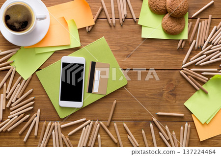 A well-organized workspace displays a cup of coffee, colorful sticky notes, a smartphone, a credit card, and freshly baked cookies. A well-organized workspace displays a cup of coffee, colorful sticky notes, a smartphone, a credit card, and freshly baked cookies. 137224464