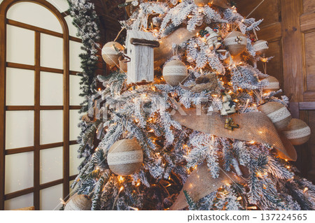 Christmas magic background. Beautiful decorated white xmas tree near huge window. Shining lights, baubles and garland. Winter holidays magic atmosphere. Modern design and decorations, copy space Christmas magic background. Beautiful decorated white xmas tree near huge window. Shining lights, baubles and garland. Winter holidays magic atmosphere. Modern design and decorations, copy space 137224565