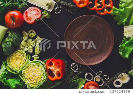 Healthy vegetarian food on black background. Fresh organic vegetables. Peppers, tomato, cabbage and other meals with empty brown clay plate, copy space Healthy vegetarian food on black background. Fresh organic vegetables. Peppers, tomato, cabbage and other meals with empty brown clay plate, copy space 137224579