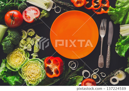 Healthy vegetable food on black background. Fresh organic peppers, tomato, cabbage and other meals with empty orange plate, copy space Healthy vegetable food on black background. Fresh organic peppers, tomato, cabbage and other meals with empty orange plate, copy space 137224589