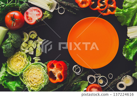 Healthy vegetable food on black background. Fresh organic peppers, tomato, cabbage and other meals with empty orange plate, copy space 137224616