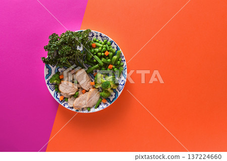 Healthy food delivery, diet nutrition. Cut organic green steamed vegetables and slices of chicken on bright geometric background, top view, copy space 137224660