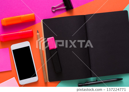 A vibrant workspace featuring a black notebook, colorful highlighters, sticky notes, a pencil, and a smartphone. The bright desk background adds energy to the setting. A vibrant workspace featuring a black notebook, colorful highlighters, sticky notes, a pencil, and a smartphone. The bright desk background adds energy to the setting. 137224771