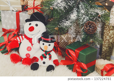 Cozy winter holidays background. Funny toy snowmen and presents waiting for christmas under decorated fir tree. Joyful and magical atmosphere of new year eve, copy space Cozy winter holidays background. Funny toy snowmen and presents waiting for christmas under decorated fir tree. Joyful and magical atmosphere of new year eve, copy space 137224781