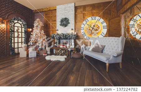 Beautiful christmas interior. Warm room with fireplace, decorated christmas tree, lots of presents and huge clock on wooden wall. Cozy home for winter holidays, copy space 137224782