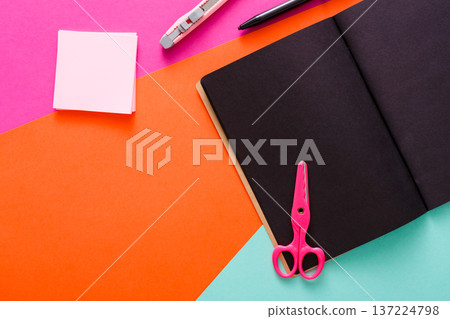 A workspace is organized with a variety of colorful stationery items. Scissors, a notebook, sticky notes, and a pen are neatly arranged on bright paper surfaces, creating a lively atmosphere. A workspace is organized with a variety of colorful stationery items. Scissors, a notebook, sticky notes, and a pen are neatly arranged on bright paper surfaces, creating a lively atmosphere. 137224798