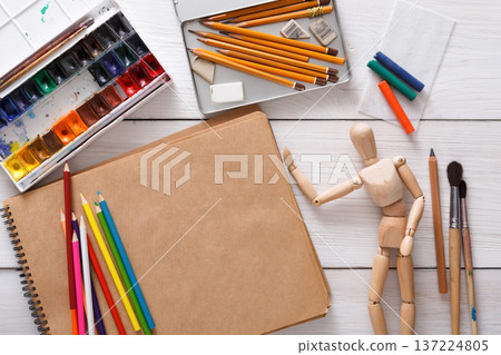 Workplace of artist. Paints, sketchbook and wooden painter man with brushes on white desk, top view, flat lay, objects Workplace of artist. Paints, sketchbook and wooden painter man with brushes on white desk, top view, flat lay, objects 137224805