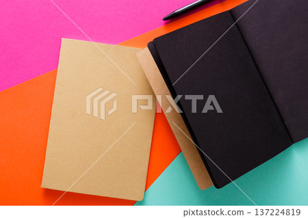 Blank notebooks in neutral colors laid on vibrant orange and pink background. A pen rests beside them, inviting creativity and inspiration for writing or planning sessions. 137224819