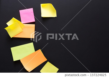 Various brightly colored sticky notes are scattered on a black surface, showcasing creativity and organization. The notes represent brainstorming, reminders, and planning for projects or tasks. 137224825