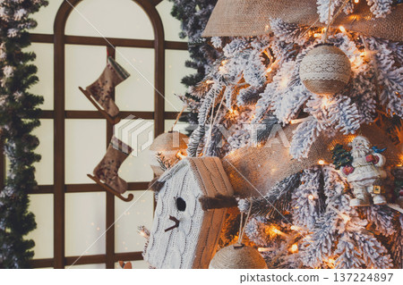 Christmas magic background. Beautiful decorated white xmas tree near huge window. Shining lights, baubles and garland. Winter holidays magic atmosphere. Modern design and decorations, copy space 137224897