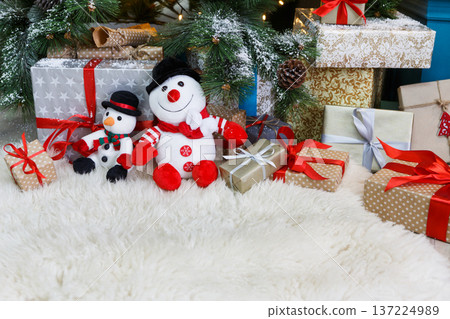 Cozy winter holidays background. Funny toy snowmen and presents waiting for christmas under decorated fir tree. Joyful and magical atmosphere of new year eve, copy space 137224989