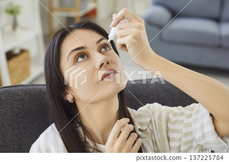 Young woman using eye drops to relieve dryness, irritation or inflammation and maintain eye health. Young woman using eye drops to relieve dryness, irritation or inflammation and maintain eye health. 137225784