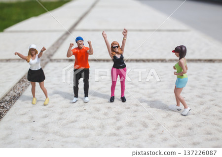 Miniature dancers raise arms energetically on outdoor concrete surface Miniature dancers raise arms energetically on outdoor concrete surface 137226087