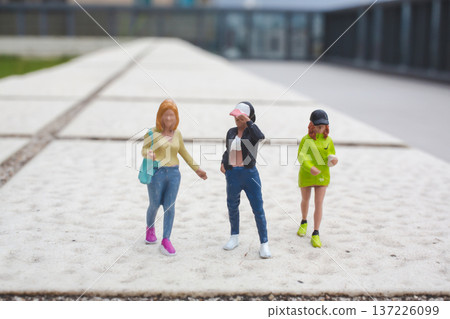 Miniature figurines appear walking together across outdoor pathway surface Miniature figurines appear walking together across outdoor pathway surface 137226099