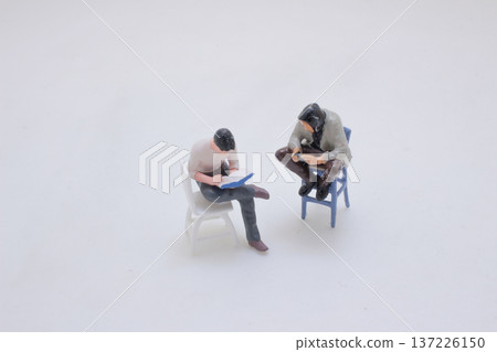 Two Miniature Figures Sit While Focusing On Handheld Objects Two Miniature Figures Sit While Focusing On Handheld Objects 137226150