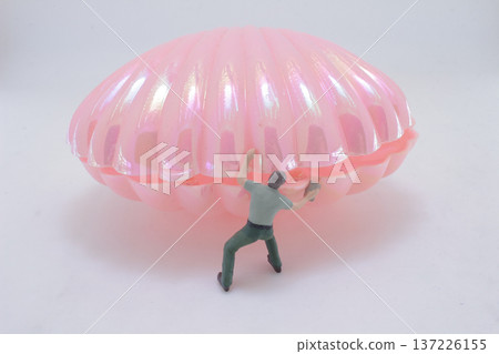 Miniature Figure Pushes Against Large Iridescent Pink Shell Miniature Figure Pushes Against Large Iridescent Pink Shell 137226155
