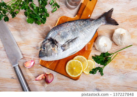 Uncooked dorado fish with lemon, garlic and parsley on wooden table Uncooked dorado fish with lemon, garlic and parsley on wooden table 137227848