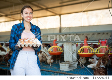 Smiling woman standing in henhouse with cardboard tray of eggs Smiling woman standing in henhouse with cardboard tray of eggs 137228011