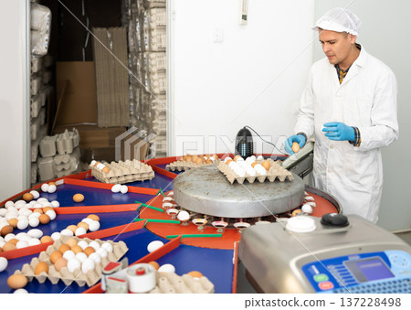 Young man farmer in white coat holding special tray with fresh chicken eggs after sorting and labeling on farm Young man farmer in white coat holding special tray with fresh chicken eggs after sorting and labeling on farm 137228498