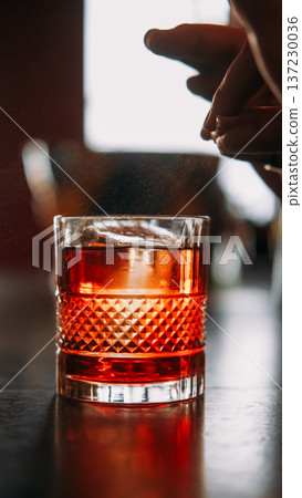 Preparing drink. Citrus cocktail. Bartender hand sprinkling orange peel juice serving negroni in wide glass. Aromatic ice beverage. Preparing drink. Citrus cocktail. Bartender hand sprinkling orange peel juice serving negroni in wide glass. Aromatic ice beverage. 137230036