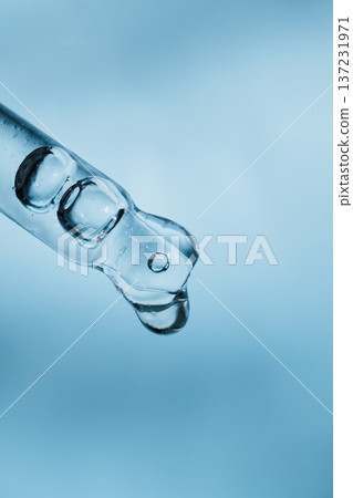 Glass pipette dropper collecting blue liquid drop on light blue background Glass pipette dropper collecting blue liquid drop on light blue background 137231971