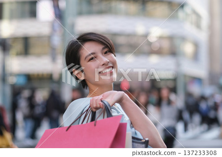 一位微笑的女士手提購物袋走在銀座街頭。 137233308