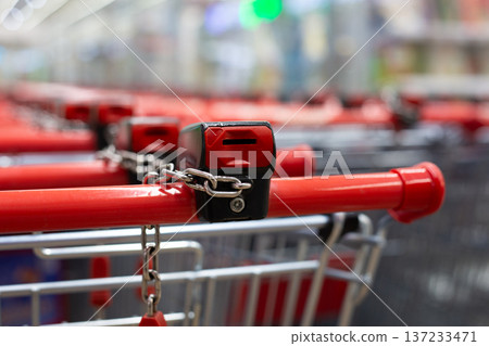 Row of self service shopping carts at grocery store. Insert coin into slot on cart handle and receive it back when you return cart to parking lot. Keep your supermarket organized with cart lock Row of self service shopping carts at grocery store. Insert coin into slot on cart handle and receive it back when you return cart to parking lot. Keep your supermarket organized with cart lock 137233471