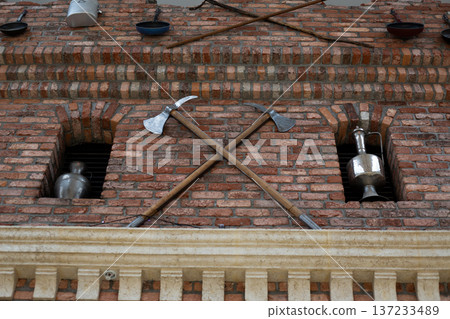Medieval workshop with crossed axes at entrance to building. Weapon making in ancient times. Military development of state through personal weapons. Axe as weapon of war. Exterior of military barrack 137233489