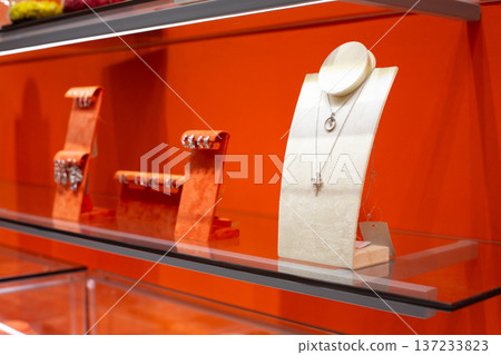 Glass shelf with the finest jewelry on display stands. Wide selection of premium jewelry in store. Elegant jewels on orange display in exclusive store of fine jewelry for women Glass shelf with the finest jewelry on display stands. Wide selection of premium jewelry in store. Elegant jewels on orange display in exclusive store of fine jewelry for women 137233823