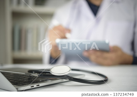 Close up medical equipment tool on notebook desk. Male practitioner holding touchpad stylus blurring back. Electronic health record smart clinic system. Wireless communication insurance idea. 137234749