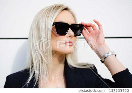 Portrait of sexy stylish woman standing in the street in black suit, wearing sunglasses on sunny spring day 137235460