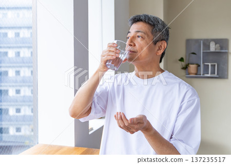 Senior man taking medicine by the window Senior man taking medicine by the window 137235517