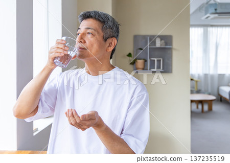 Senior man taking medicine by the window Senior man taking medicine by the window 137235519