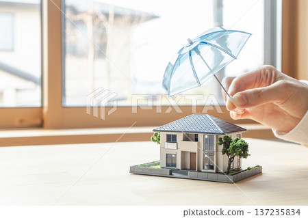 A model of a house safely protected by an umbrella. Image material for home fire insurance and earthquake insurance. A model of a house safely protected by an umbrella. Image material for home fire insurance and earthquake insurance. 137235834