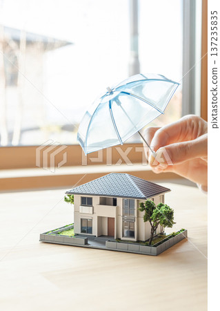 一座房屋模型,在雨傘的保護下安全無虞。可用於家庭火災保險和地震保險的圖片素材。 一座房屋模型,在雨傘的保護下安全無虞。可用於家庭火災保險和地震保險的圖片素材。 137235835