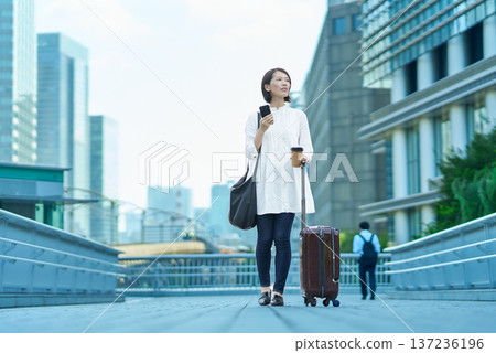 城市裡，一位女士提著行李箱，手裡拿著智慧型手機。 137236196