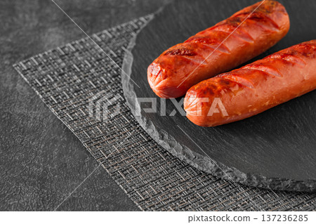 Grilled sausages fried two, on slate stone plate round, dark background, selective focus Grilled sausages fried two, on slate stone plate round, dark background, selective focus 137236285