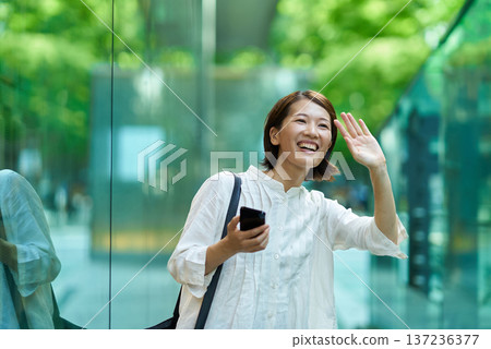 A woman holding a smartphone and waving in the street 137236377