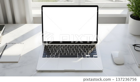 Modern minimalist workspace with a laptop, blank screen, and natural light on a marble desk. 137236756