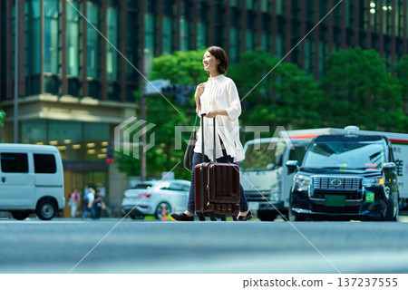 一個女人帶著手提箱在城市裡行走 137237555