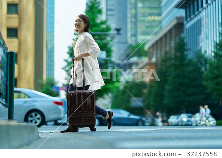 一個女人帶著手提箱在城市裡行走 137237558