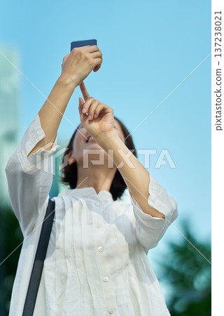 A woman holding up a smartphone in the city on a sunny day 137238021