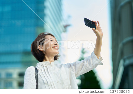 A woman holding up a smartphone in the city on a sunny day A woman holding up a smartphone in the city on a sunny day 137238025