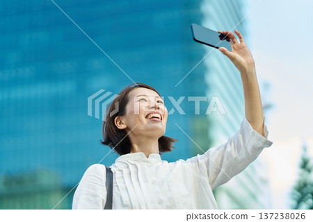 A woman holding up a smartphone in the city on a sunny day 137238026
