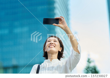A woman holding up a smartphone in the city on a sunny day 137238027