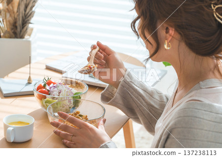 一位女士坐在客廳的桌旁，吃著格蘭諾拉麥片和沙拉。 137238113