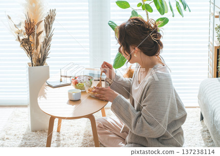 一位女士坐在客廳的桌旁，吃著格蘭諾拉麥片和沙拉。 137238114