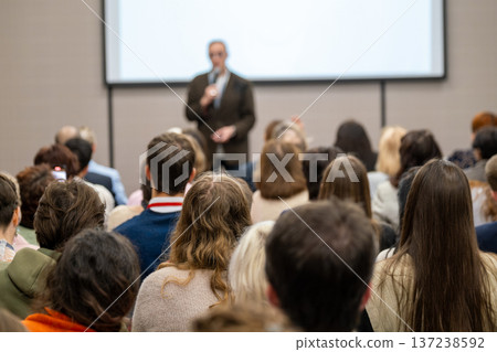 Audience listening to speaker presentation at business conference, attendees using phones to record 137238592