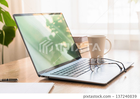 Laptop, eyeglasses, coffee, and books on a desk, creating a productive home office and remote workstation setup. Remote work concept 137240839